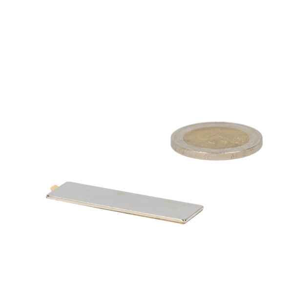 Silver neodymium block magnet 40x12x1 mm next to coin for bowl with powerful magnetic solution